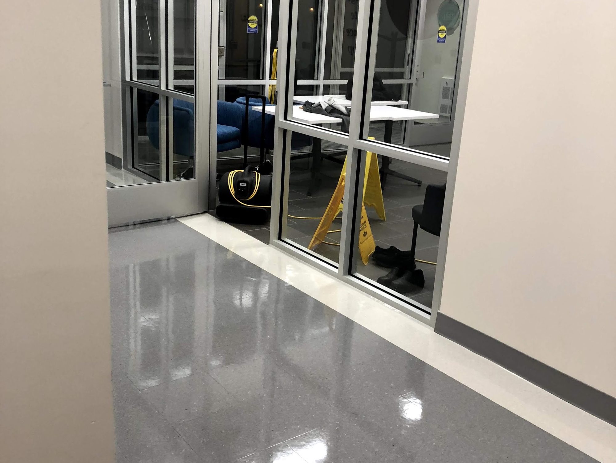 Polished corridor floor outside a glass-walled meeting room, wet-floor sign still out