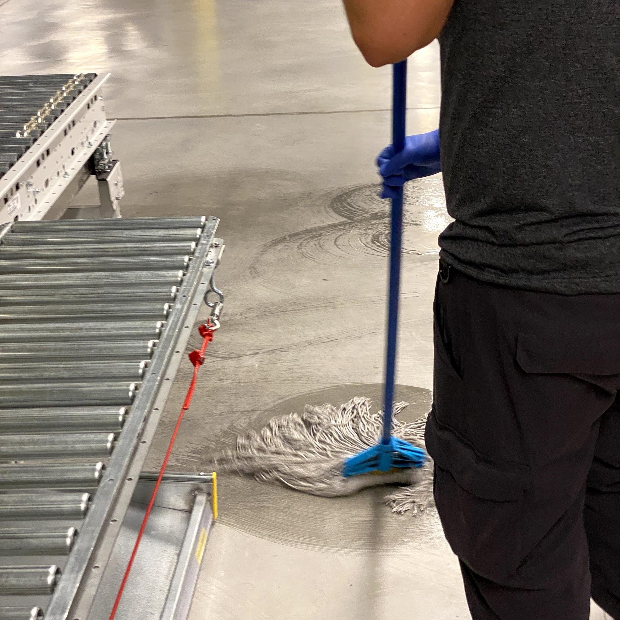 Damp mopping sealed concrete beside a conveyor line in a warehouse