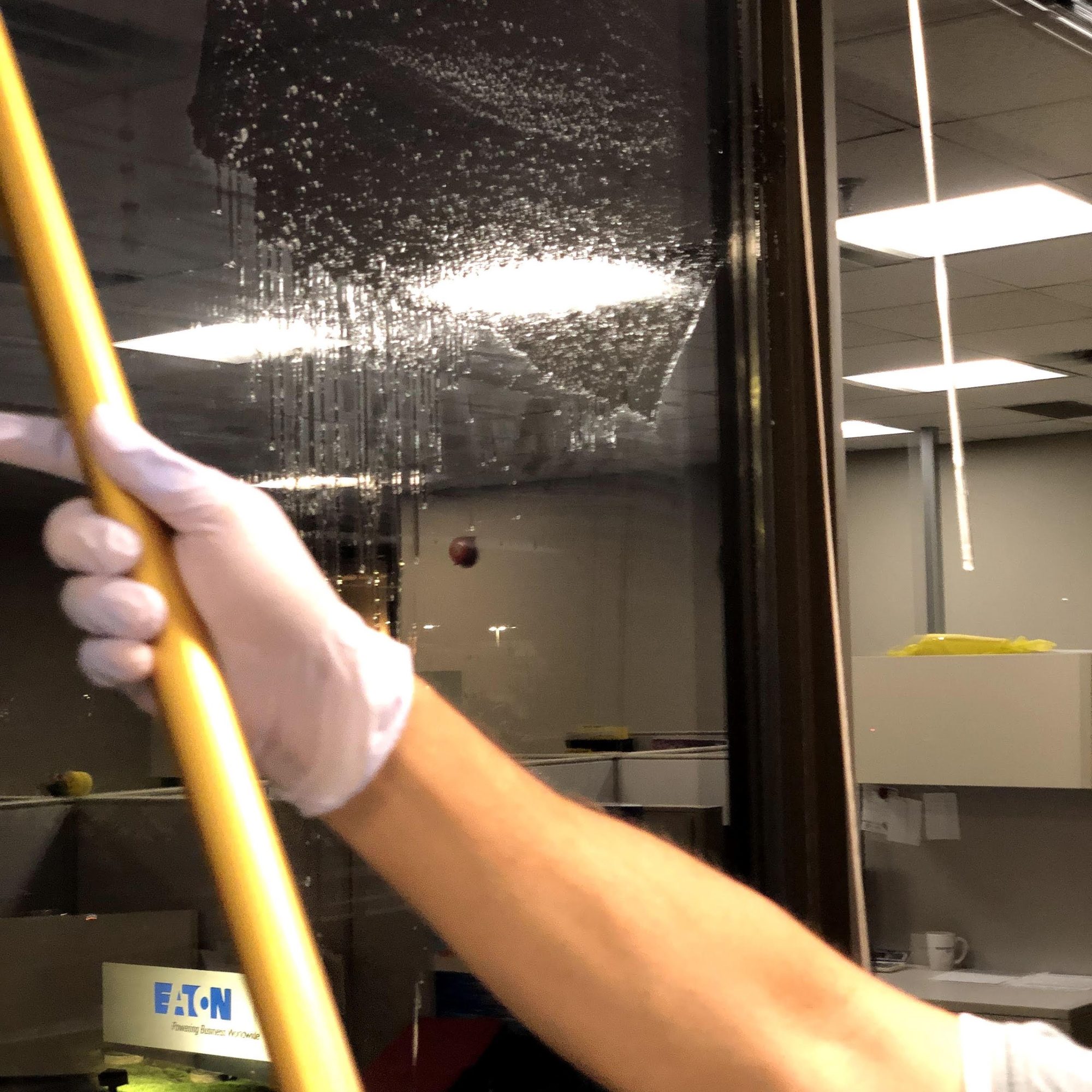 A gloved hand pulling a squeegee down interior office glass